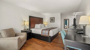 A hotel room with a bed, a desk, a chair, and a nightstand. - Pine Tree Inn (Medford)