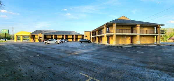 Un motel con varias habitaciones, un estacionamiento y un pequeño edificio con balcón.