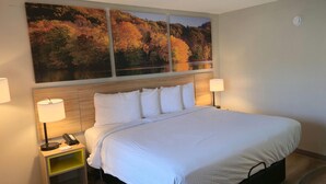 Habitación de hotel con una cama grande, dos lámparas de noche, una mesita con teléfono y un cuadro colgado en la pared.