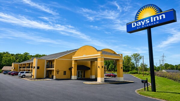 Un hotel Days Inn by Wyndham con fachada amarilla, entrada cubierta y estacionamiento.