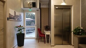 A modern lobby with a large door, a red chair, a small table, and an elevator. - LeNotti Verona (Verona)