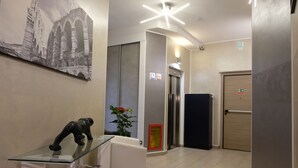 A hallway with a glass table, a sculpture, a framed picture, and an elevator. - LeNotti Verona (Verona)
