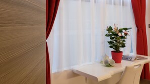 A modern room with a wooden door, red curtains, a white desk with a potted plant, and a red pillow on a chair. - LeNotti Verona (Verona)