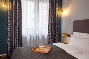 A neatly made bed with a tray of a beverage and glasses, a bedside lamp, and curtains with a leaf pattern. - My Place (Hamburg)