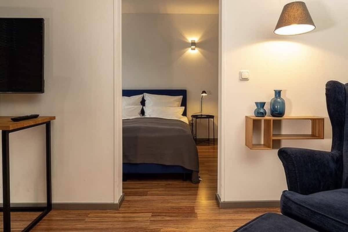 A hotel room with a bed, bedside table, lamp, and a TV mounted on the wall.