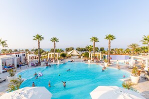 Une grande piscine extérieure entourée de palmiers et de chaises longues, avec une vue sur la mer en arrière-plan.