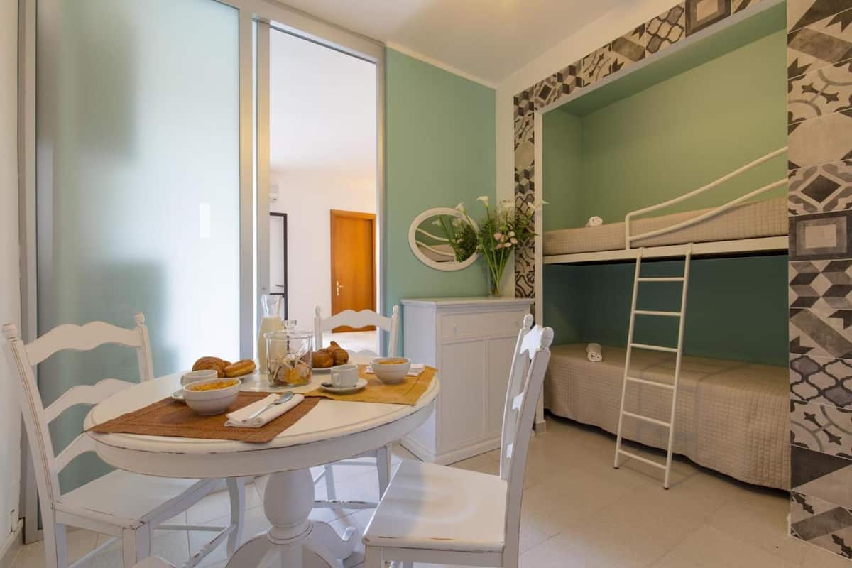 A compact room with a bunk bed, a dining table with chairs, and a small cabinet.