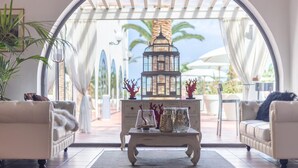 Una sala de estar acogedora con un sofá blanco, una mesa de centro con objetos decorativos y vistas a un jardín a través de un arco.