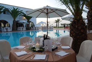 A poolside dining setup with tables, chairs, and umbrellas.