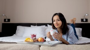 Una persona acostada en una cama con una bandeja de comida y una taza.