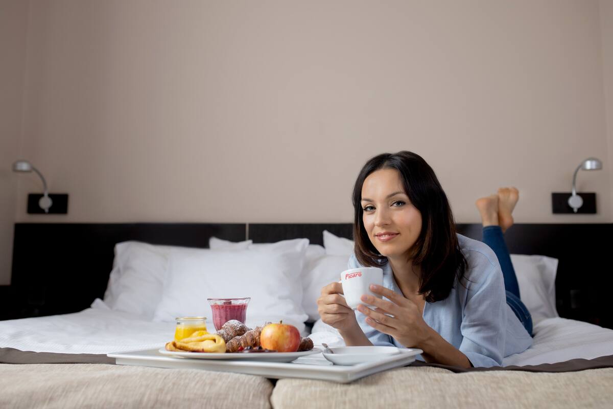 Eine Person liegt im Bett, neben sich ein Tablett mit Essen und einer Tasse.