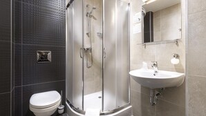 Un baño moderno con ducha de vidrio, lavamanos blanco y retrete.