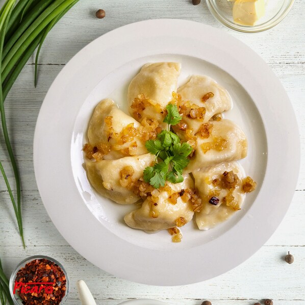 Un plato de dumplings adornado con cebollas y perejil, sobre un plato blanco.