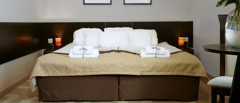 A hotel room with a large bed, two bedside lamps, a small table with a vase, and a wall-mounted picture.