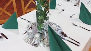 A table set for a meal with a decorative glass centerpiece containing green foliage and a candle.