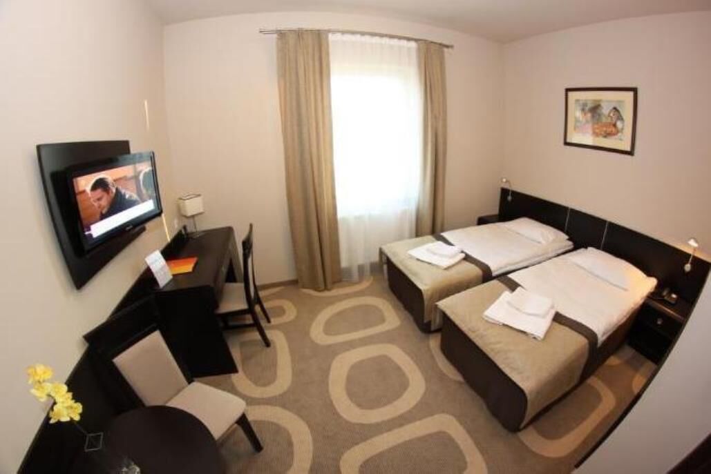 A hotel room with two beds, a desk, a TV, and a window with curtains.