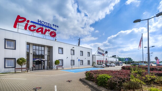 A hotel named 'Hotel Piccaro' with a modern facade, a covered entrance, and a parking area with blue markings.