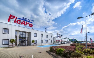 Un hotel llamado 'Hotel Piccaro', con una fachada moderna, un acceso cubierto y un área de estacionamiento con marcas azules.