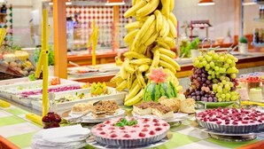 A buffet with various food items including bananas, grapes, watermelon, and desserts.