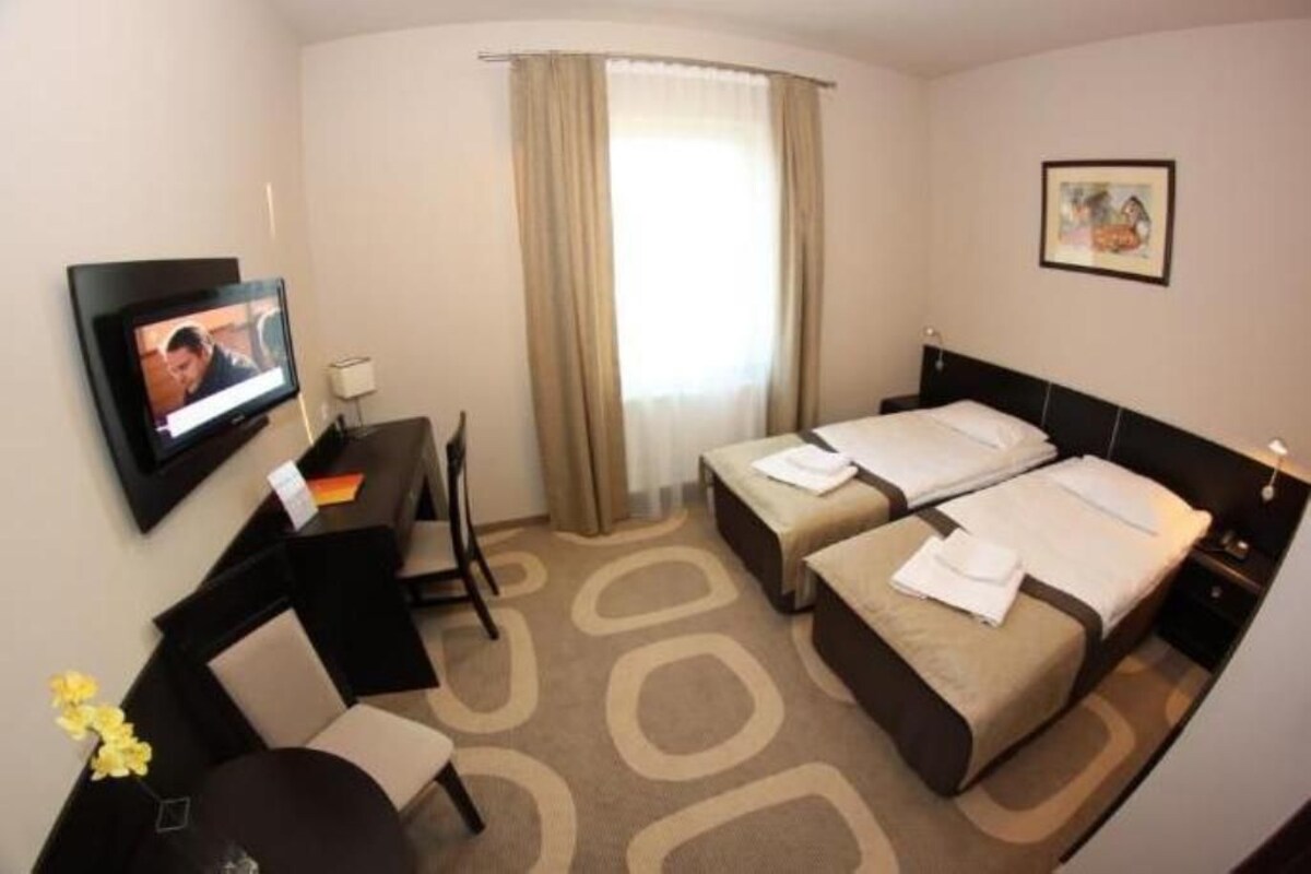 A hotel room with two beds, a desk, a TV, and a window with curtains.