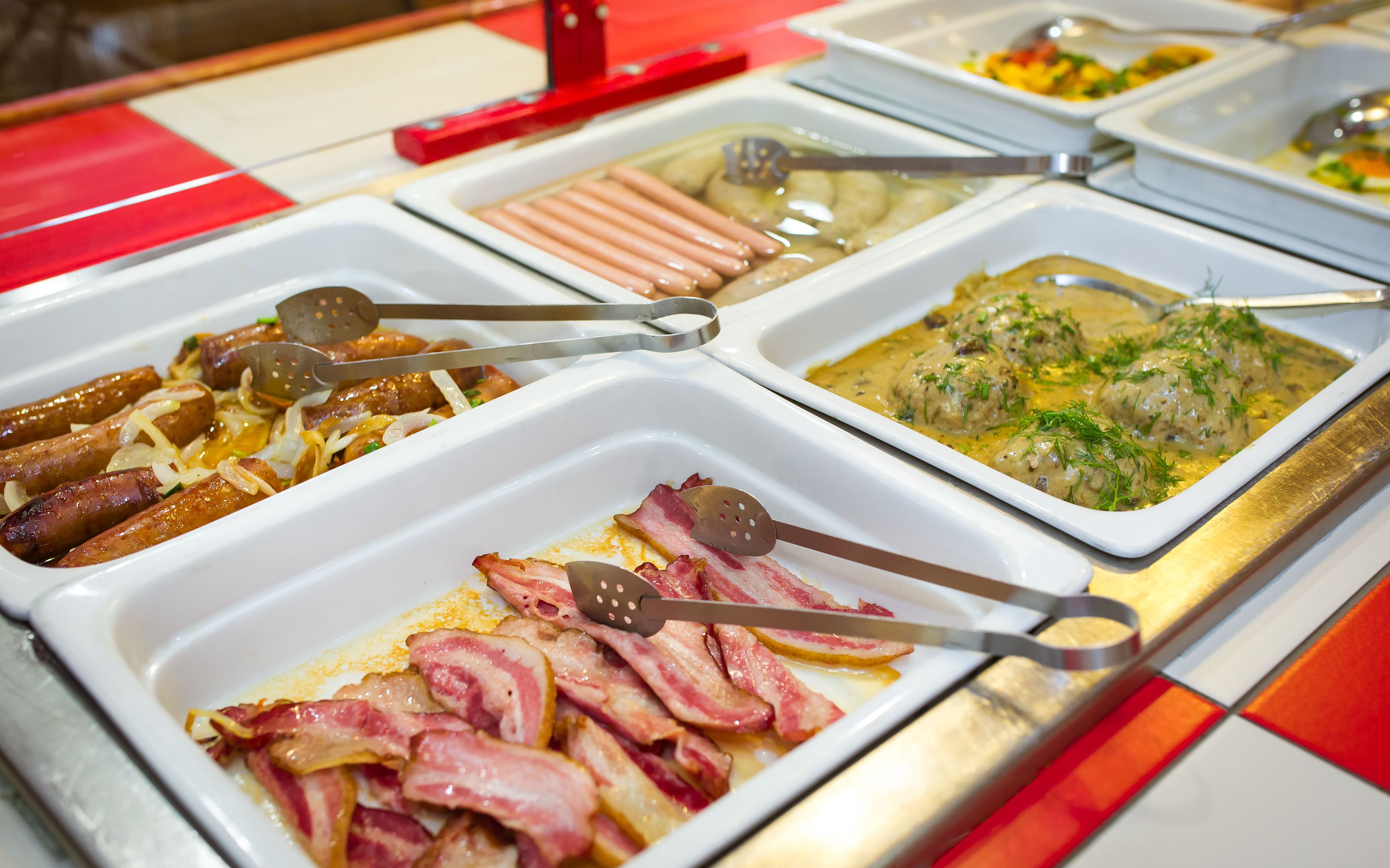 Ein Buffet mit verschiedenen Speisen, darunter Würstchen, Speck und eine cremige Mahlzeit.