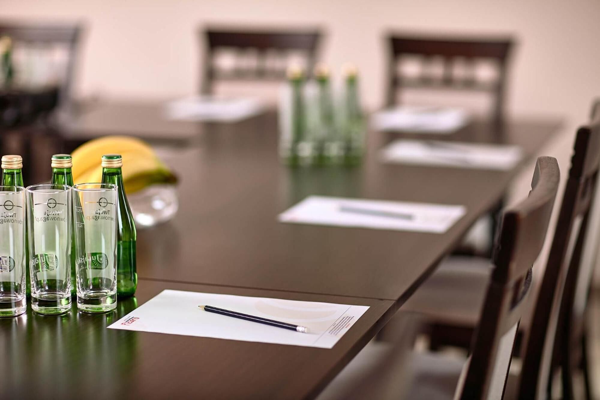 Una mesa de conferencias con botellas verdes, un plátano y un cuaderno con un bolígrafo.