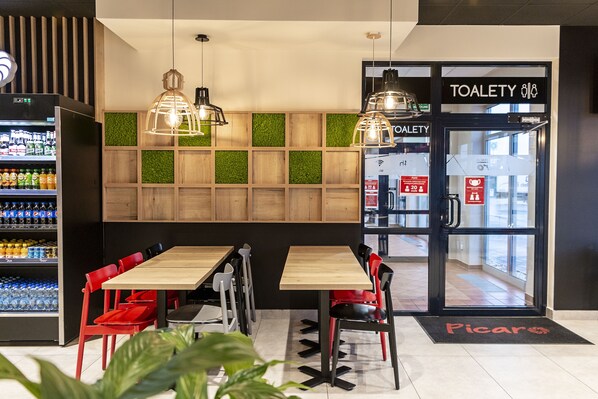 A restaurant interior with wooden tables and red chairs, a refrigerated display case, and a 'TOALETY' sign.