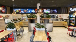 Un restaurant avec une longue table en bois, des chaises rouges et grises, et un comptoir où est affiché le menu.