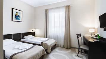 Una camera d'albergo con due letti, una scrivania con sedia, una televisione e una finestra con tende.