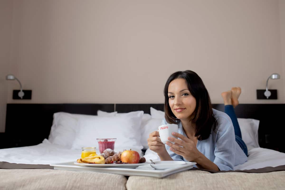 A person lying on a bed with a tray of food and a cup.