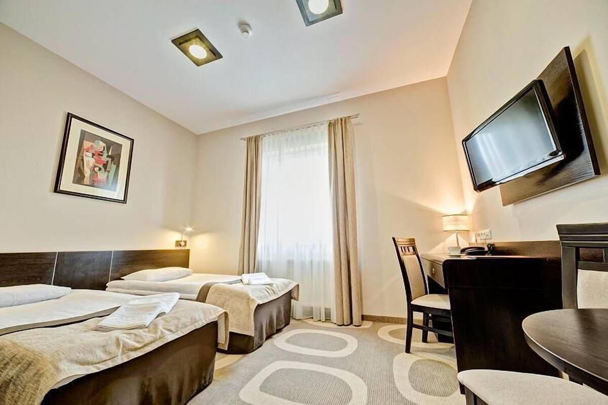 A hotel room with two beds, a desk, a chair, a TV, and a window with curtains.