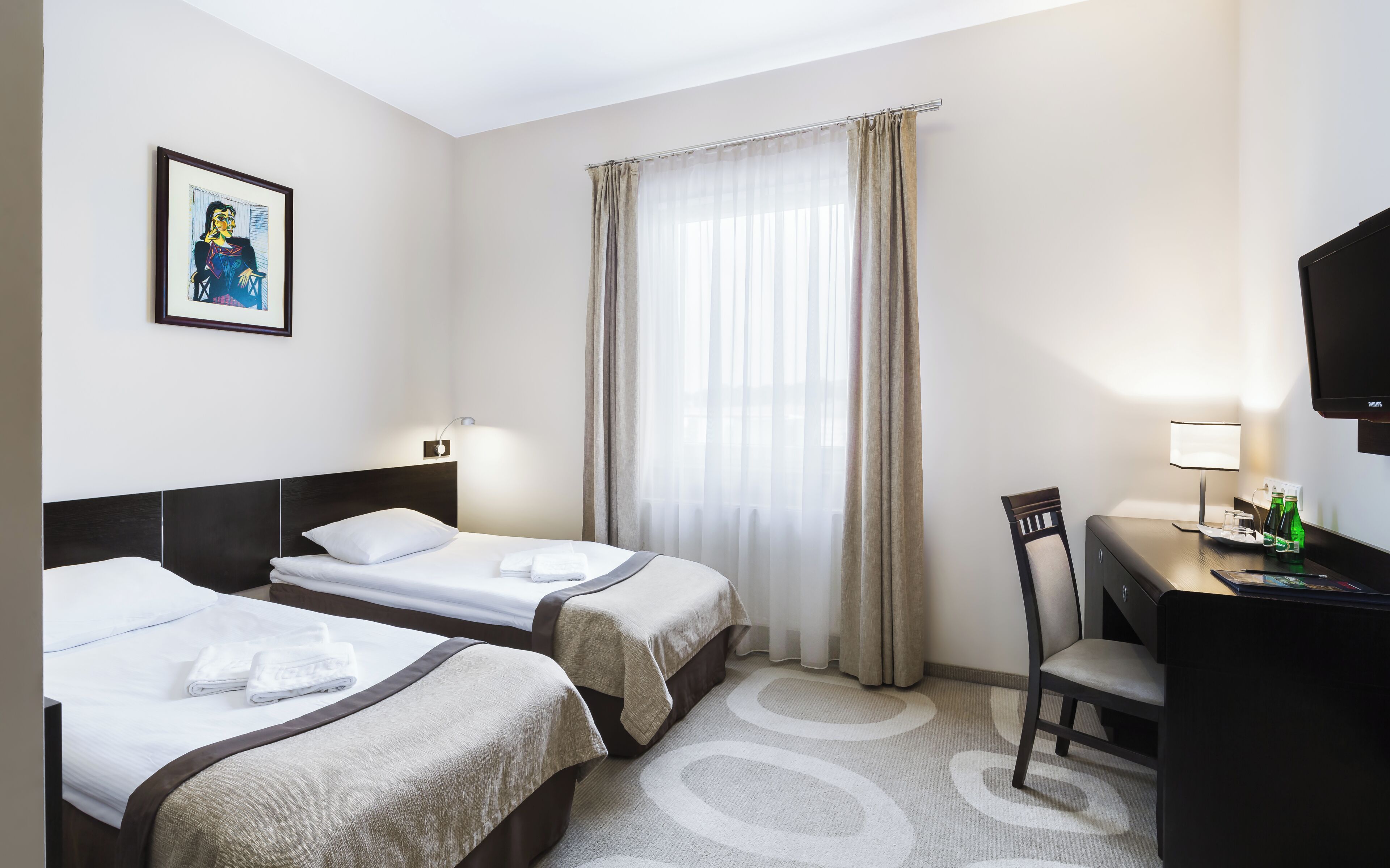 A hotel room with two beds, a desk with a chair, a television, and a window with curtains.