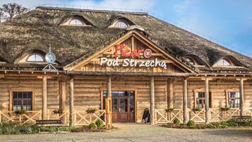 Un bâtiment en bois avec un toit de chaume, une enseigne indiquant « Picar Pod Strzecha », et une zone d’entrée pavée avec des bancs et des plantes en pot.