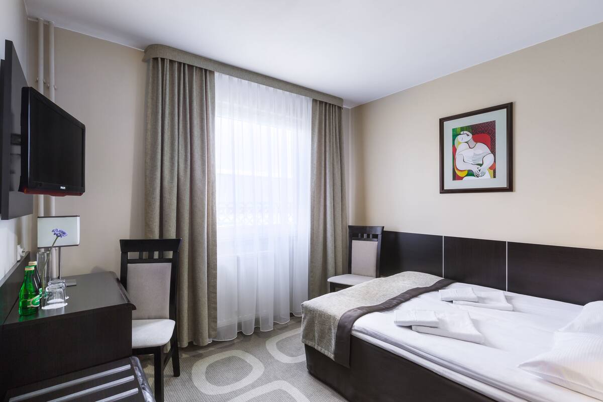 Una habitación de hotel con cama, escritorio y silla, televisión y ventana con cortinas.