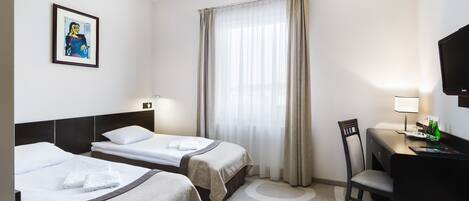 A hotel room with two beds, a desk with a chair, a television, and a window with curtains.