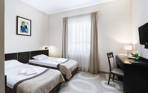 A hotel room with two beds, a desk with a chair, a television, and a window with curtains.