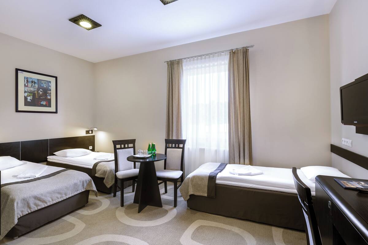 Habitación de hotel con dos camas, una mesita con sillas, televisión y ventana con cortinas.