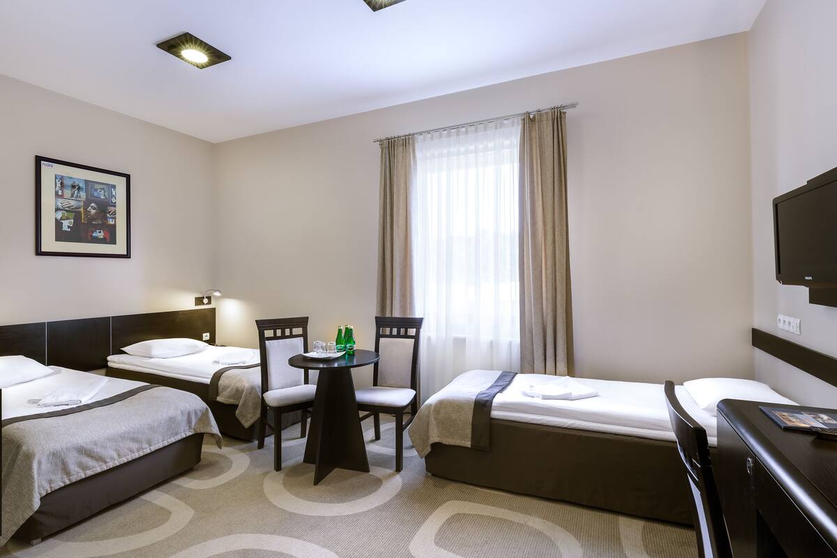 Habitación de hotel con dos camas, una mesita con sillas, televisión y ventana con cortinas.