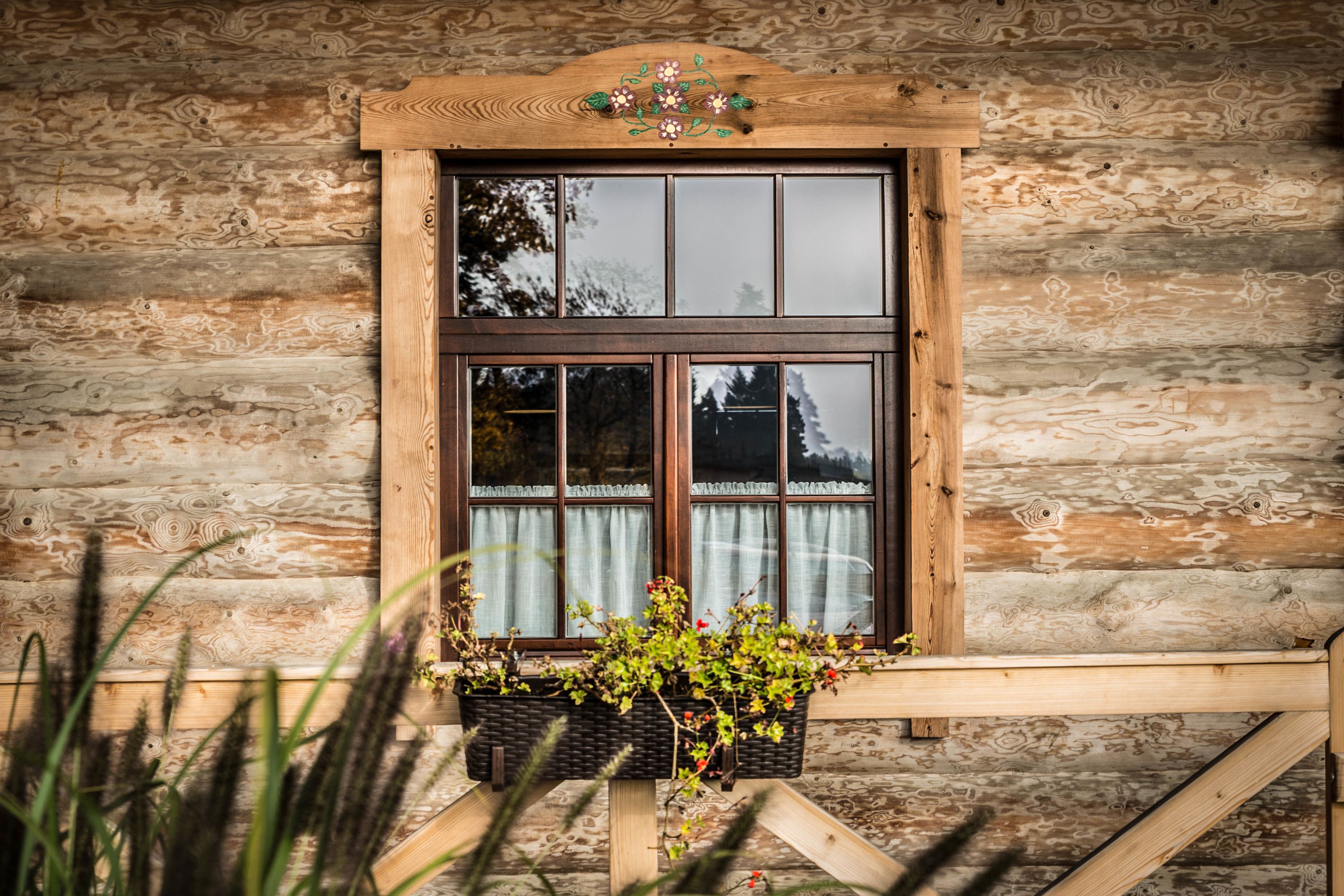 A wooden cabin with a window featuring a decorative top and a basket of plants.