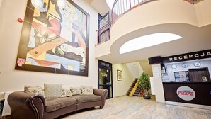 Un hall de hotel con un cuadro abstracto de gran tamaño, una recepción, una escalera y un sofá.