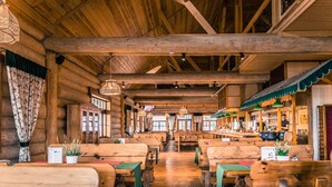 Un restaurante de estilo cabaña de troncos con bancos y mesas de madera, una zona de bar y un techo alto con vigas a la vista.