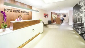Un área de recepción de hotel moderna con un mostrador de madera, una recepcionista y un cartel grande en la pared.