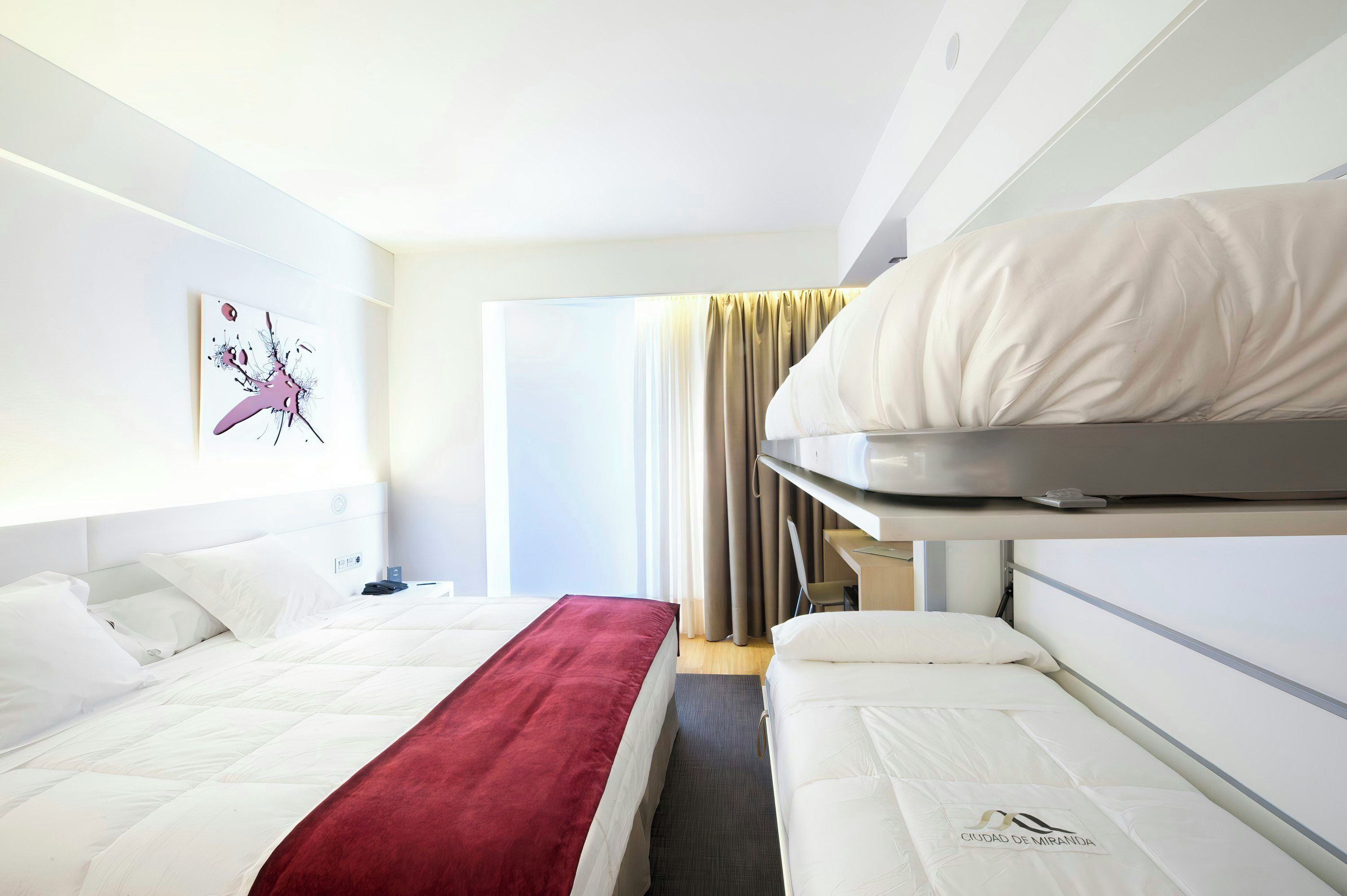 Ein Hotelzimmer mit Bett, Schreibtisch, Stuhl und einem Fenster mit Vorhängen.