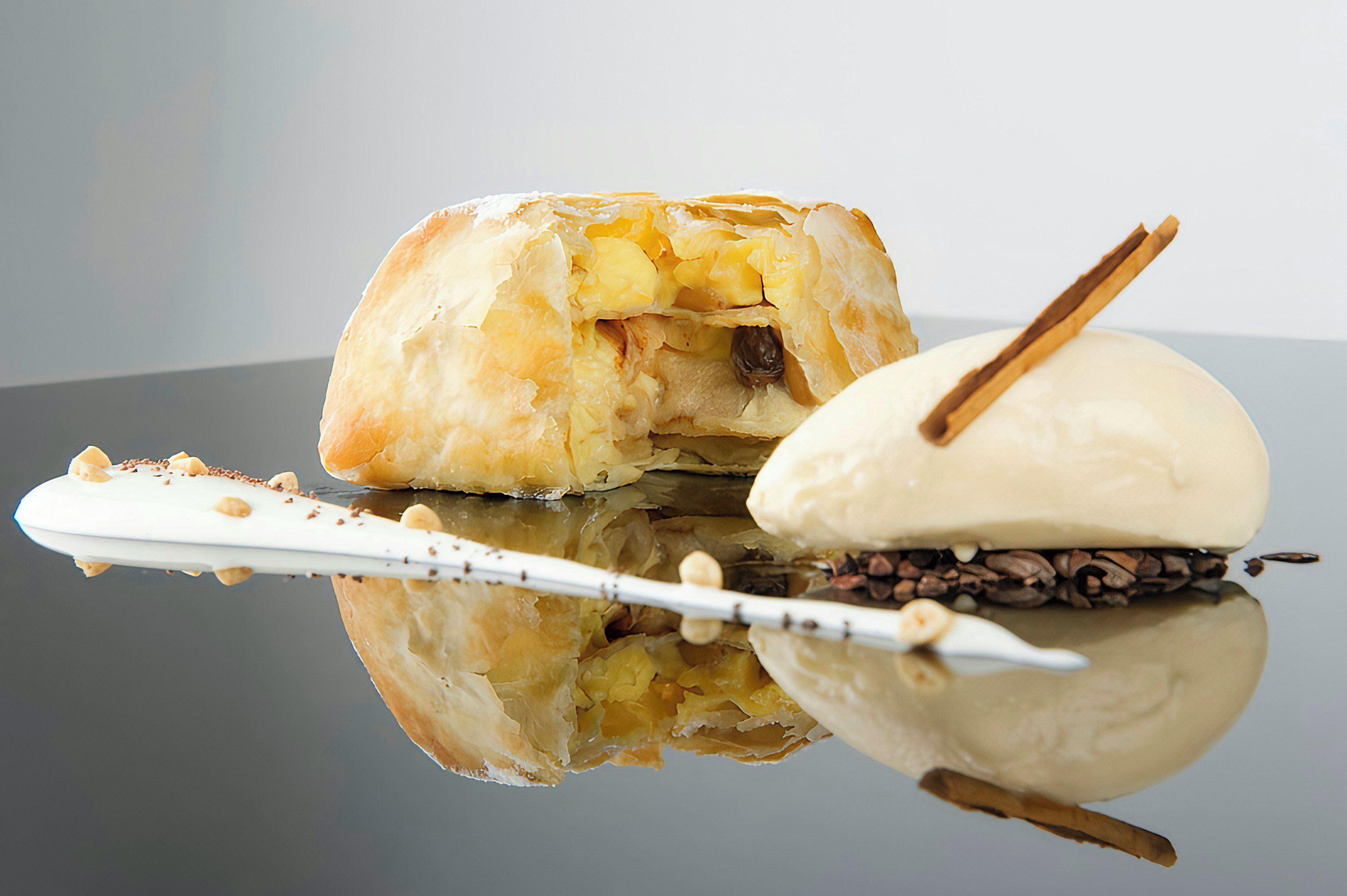 A dessert with a pastry and a scoop of ice cream on a reflective surface.