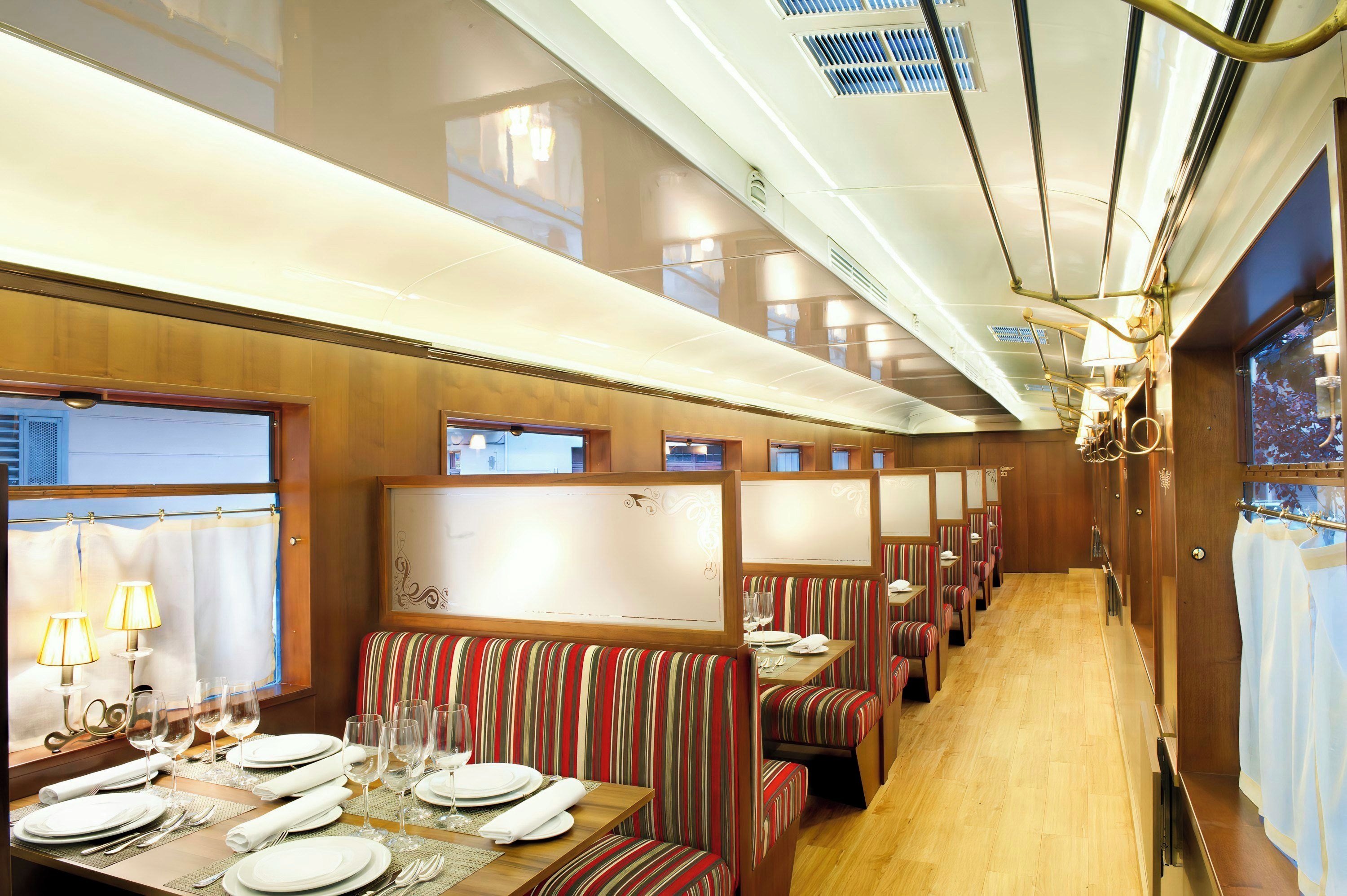 A dining car with striped upholstered booths, tables set for dining, and overhead lighting.