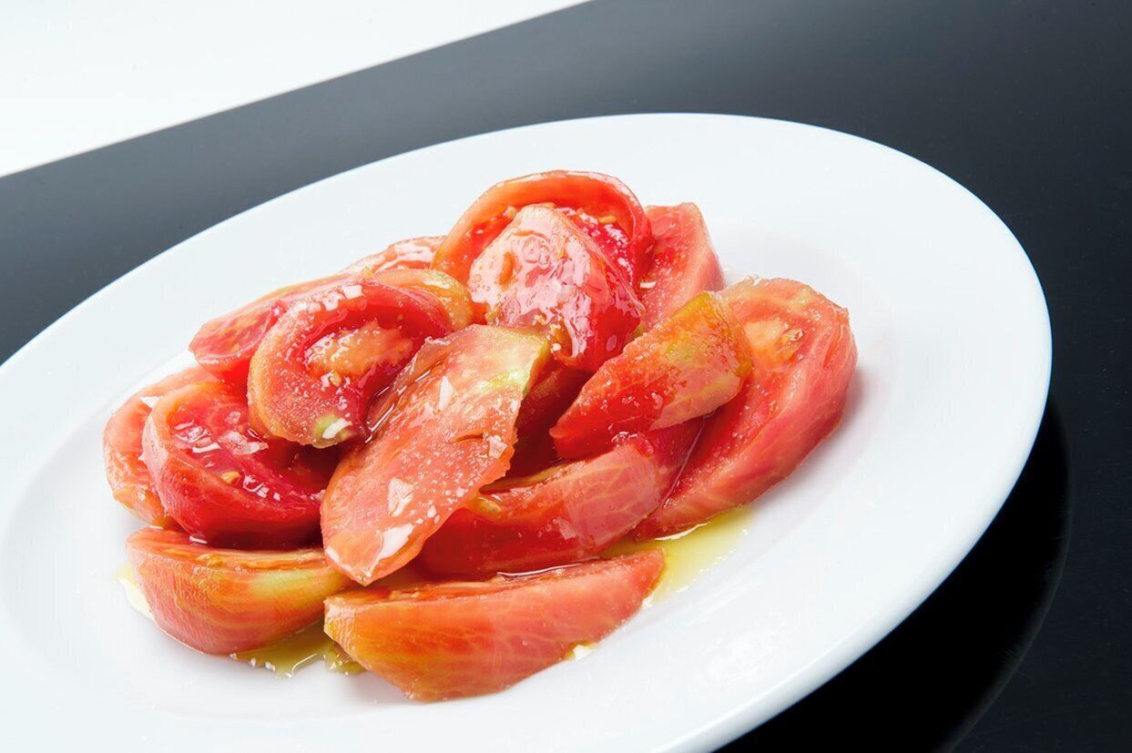 Un plato blanco con rodajas de tomate y aceite de oliva sobre una superficie negra.