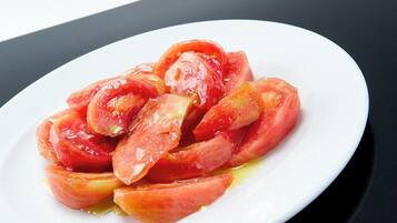Un plato blanco con rodajas de tomate y aceite de oliva sobre una superficie negra.