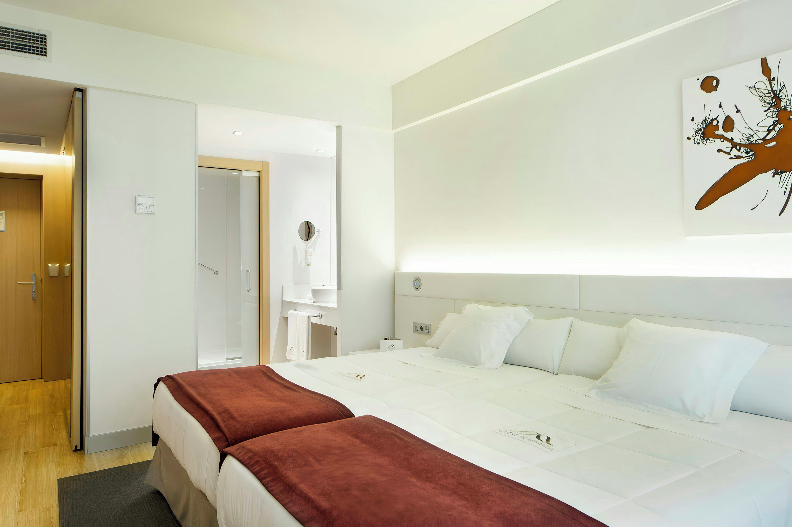 Ein Hotelzimmer mit einem Bett, einem Nachttisch, einem Spiegel und einem an der Wand hängenden Kunstwerk.