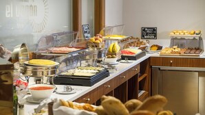Un bufé con diversas opciones de comida, entre ellas frutas, pasteles y un cartel que indica las opciones de desayuno.