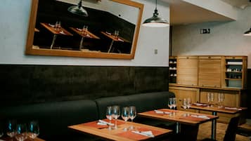 A restaurant interior with wooden tables, black cushioned seating, and pendant lighting.